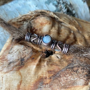 Può includere: Un perno per dreadlock in filo di rame con un accento di pietra di luna bianca. Il perno è avvolto attorno a una dreadlock marrone.