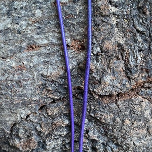 Puede incluir: Dos hebras de cord&oacute;n de cuero morado, tendidas sobre una superficie de madera marr&oacute;n rugosa.