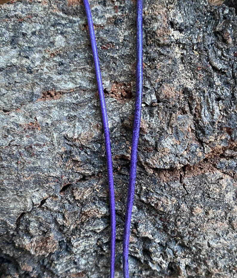 Puede incluir: Dos hebras de cord&oacute;n de cuero morado, tendidas sobre una superficie de madera marr&oacute;n rugosa.