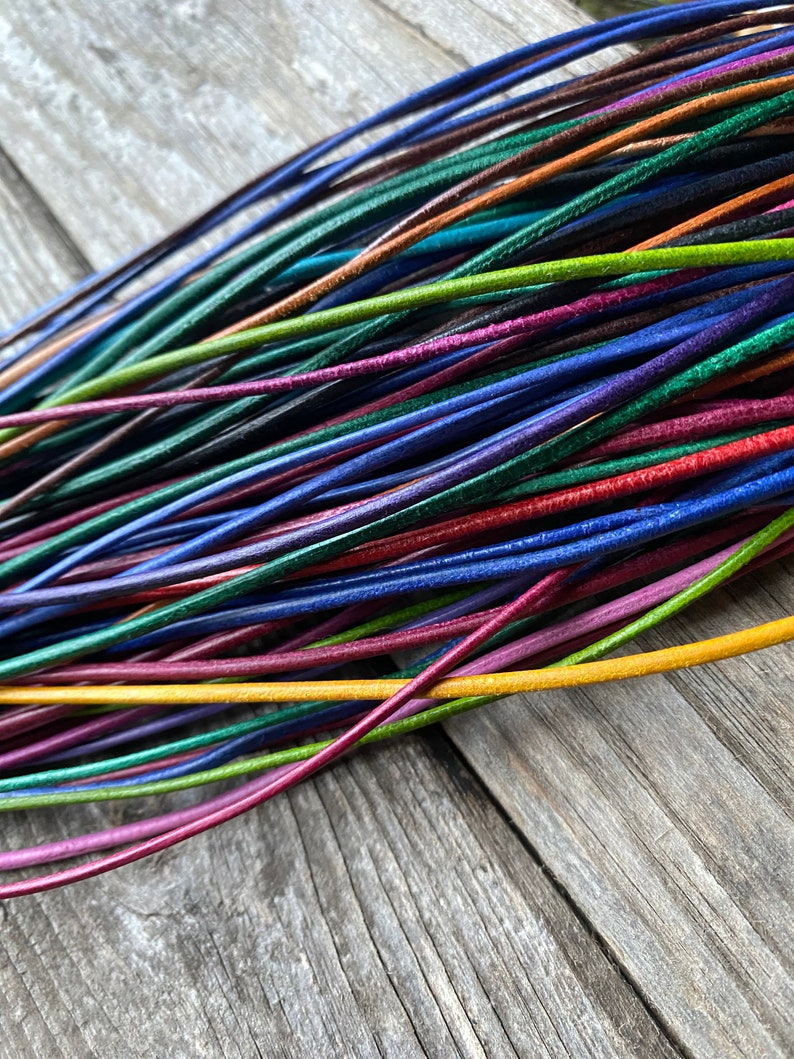 Puede incluir: Una colecci&oacute;n de cordones de cuero de colores en varios tonos de azul, verde, rojo, amarillo y marr&oacute;n. Los cordones est&aacute;n dispuestos en forma de abanico y est&aacute;n sobre una superficie de madera.