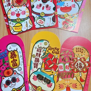 May include: Red and gold Chinese New Year envelopes with a cartoon cat design. The envelopes feature the text "Good Luck", "Get Rich", "Money", "Happy", and "Lucky Cat".