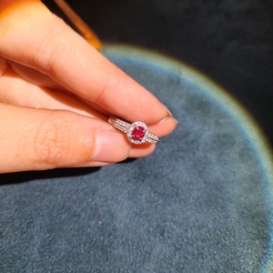 May include: A silver ring with a red gemstone surrounded by smaller white gemstones.