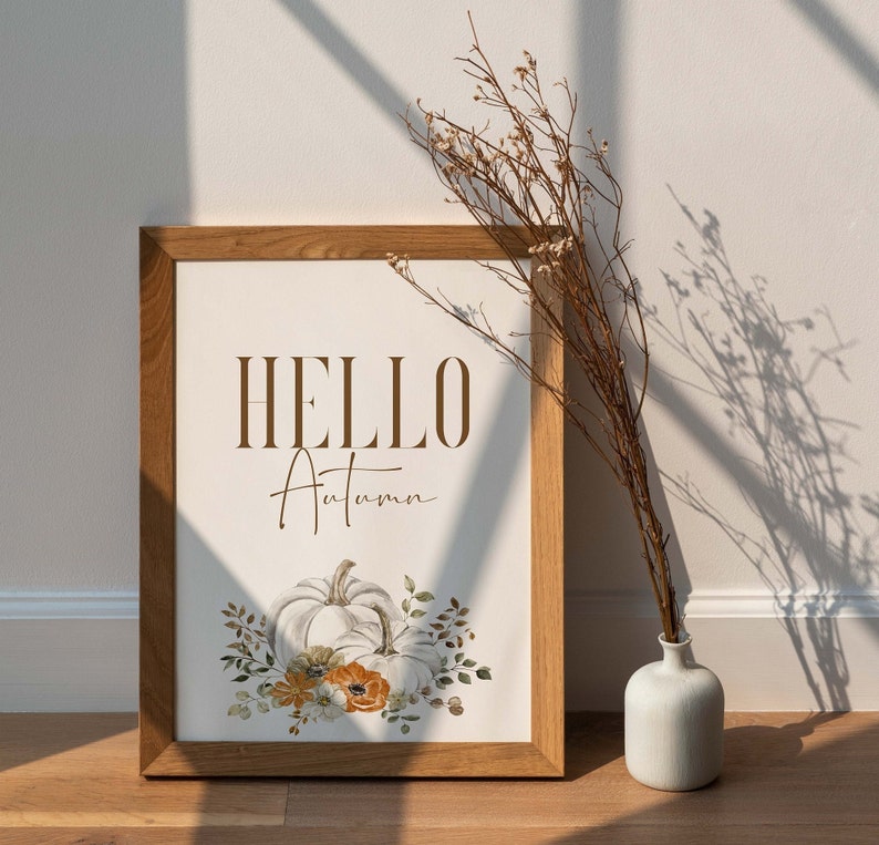 May include: A framed print with the text "HELLO Autumn" in brown lettering. The print features a watercolour illustration of white pumpkins with orange and yellow flowers and green leaves.