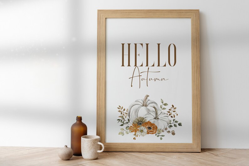 May include: A framed print with the text "HELLO Autumn" in brown lettering. The print features a watercolour illustration of two white pumpkins with orange and white flowers and green leaves.