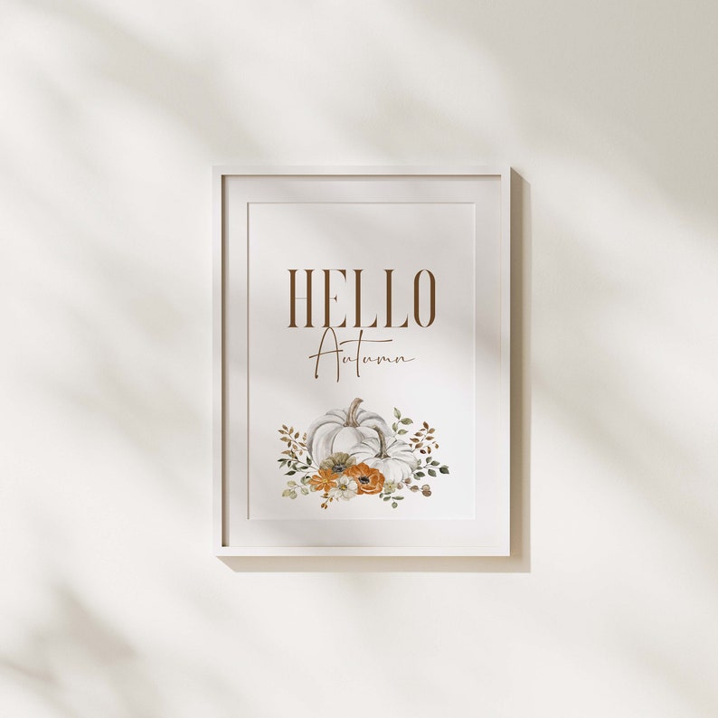 May include: A white framed print with the text "HELLO Autumn" in brown lettering. The print features a watercolour illustration of two white pumpkins with orange and white flowers and green leaves.