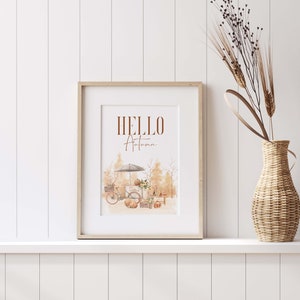 Peut inclure: Une impression encadr&eacute;e avec le texte "HELLO Autumn" en lettres brunes. L'impression pr&eacute;sente une illustration aquarelle d'un v&eacute;lo avec une verri&egrave;re, des citrouilles et des feuillages d'automne.
