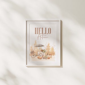 Peut inclure: Une impression encadr&eacute;e blanche avec le texte "HELLO Autumn" en lettres brunes. L'impression pr&eacute;sente une illustration aquarelle d'un v&eacute;lo avec un chariot rempli de citrouilles et de fleurs, sur fond de for&ecirc;t d'automne.