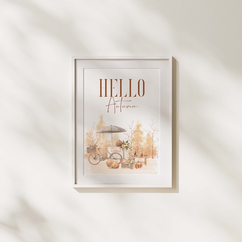 Peut inclure: Une impression encadr&eacute;e blanche avec le texte "HELLO Autumn" en lettres brunes. L'impression pr&eacute;sente une illustration aquarelle d'un v&eacute;lo avec un chariot rempli de citrouilles et de fleurs, sur fond de for&ecirc;t d'automne.