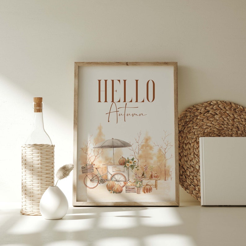 Peut inclure: Une illustration aquarelle d'une sc&egrave;ne d'automne avec un chariot en bois rempli de citrouilles et de courges. Le chariot est tir&eacute; par un v&eacute;lo avec un panier &agrave; l'avant. Le texte "HELLO Autumn" est &eacute;crit en lettres brunes en haut de l'image.