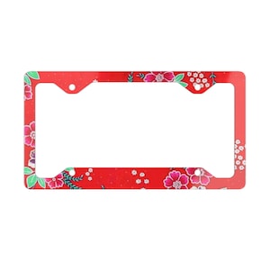 May include: A red license plate frame with a floral pattern. The frame features a repeating design of pink and white flowers with green leaves. The background is a solid red color.