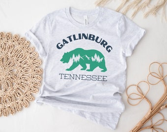 以下が含まれることがあります： グレーのTシャツに、緑色の熊のシルエットと「Gatlinburg Tennessee」という文字がネイビーブルーで書かれています。