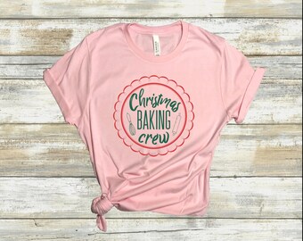 Pode incluir: Camiseta rosa com um design circular vermelho e verde que diz "Christmas Baking Crew".