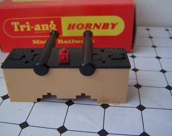 Könnte beinhalten: Eine braune Spielzeugkanone aus Plastik mit zwei schwarzen Läufen und einem roten Stein oben. Die Kanone ist mit "Tri-ang Hornby Model Railway" beschriftet.