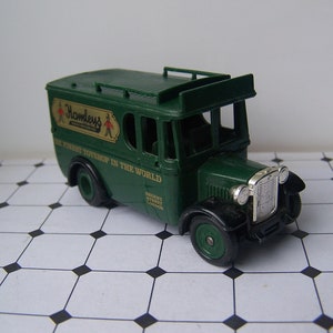 May include: A green toy delivery truck with the words "Hamleys The Finest Toyshop In The World" on the side. The truck has a silver grill and headlights.