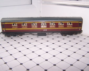 May include: A red and brown model train car with a gray roof and yellow accents. The car has windows and the text "L.M.S." on the side. The car is numbered "3" on one end and "1" on the other.
