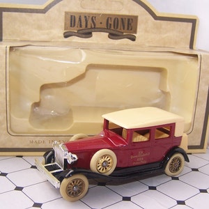 May include: A red and cream vintage car model in a box with the words "Days Gone" on the box. The car has a cream roof and black wheels. The car has the text "H.M. Queen Elizabeth II H.R.H. Prince Philip" on the side.