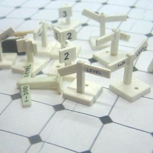 Pode incluir: Uma coleção de pequenos sinais em miniatura de plástico branco com bases quadradas e topos em forma de T. Alguns sinais apresentam a palavra LEVEL, enquanto outros exibem números como 1, 2, 3, 5 ou rácios como 1-20 e 1-300 em tinta preta.