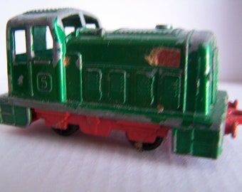 May include: A green toy train engine with a silver roof and red wheels. The engine has a number "5" on the side.