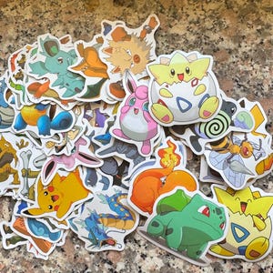 Può includere: Una collezione di adesivi fustellati colorati con vari personaggi dei cartoni animati. Gli adesivi mostrano una varietà di creature in colori vivaci, tra cui giallo, blu, verde e rosa. Gli adesivi sono probabilmente per scopi decorativi.