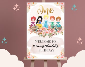 Könnte beinhalten: Ein weißes bedruckbares Schild mit goldenen Glitzerakzenten und floralen Designs. Das Schild lautet "Eins" und "Willkommen zum Geburtstag von Prinzessin Chantal". In der Mitte des Schildes befinden sich fünf Comic-Prinzessinnen.
