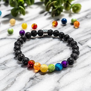 May include: A black lava stone bracelet with a rainbow of chakra beads. The bracelet features a series of black, porous lava beads and seven colorful gemstone beads. The colorful beads are red, orange, yellow, green, blue, and purple.
