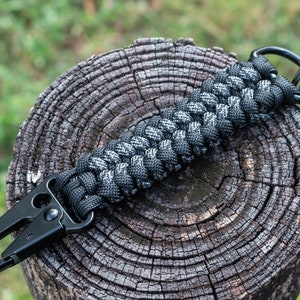 May include: A black and grey paracord keychain with a black metal carabiner and a black metal key ring.