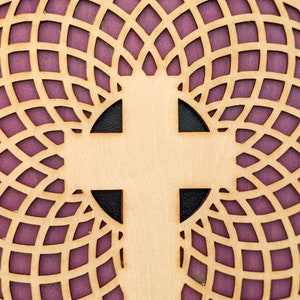 Pode incluir: Um círculo de madeira com um padrão geométrico e uma cruz branca no centro. O círculo é de cor castanho claro e o padrão é de cor roxo escuro.