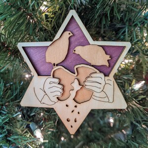 May include: A wooden star-shaped Christmas ornament with a purple background. Two birds are perched on a piece of bread, which is being held by two hands.