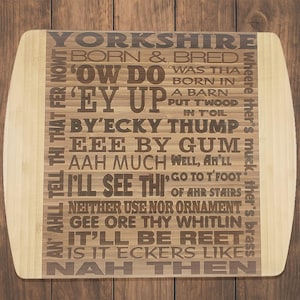 Peut inclure: Une planche à découper en bambou brun avec une bordure blanche. La planche est décorée d'un texte noir qui dit "Yorkshire Born & Bred 'Ow Do Was Tha Born In A Barn Put Tw'ood In Toil Ey Up By'Ecky Thump Eee By Gum Aah Much Well, Ah'll I'll See Thi' Go To T'Foot Of Ahr Stairs Neither Use Nor Ornament Gee Ore Thy Whitlin It'll Be Reet Is It Eckers Like Nah Then Wheere Ther's Muck, Ther's Brass".