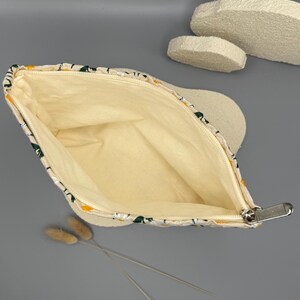 May include: A zippered pouch with a daisy floral pattern on a cream background. The interior is a light yellow color. The zipper is silver. The pouch is open, revealing the inside. Dried flowers are in the foreground.