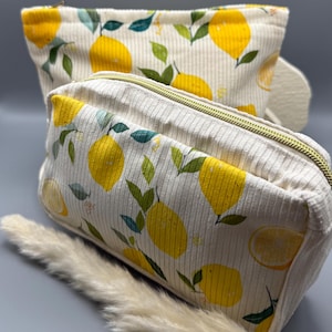 Könnte beinhalten: Zwei Kosmetiktaschen aus cremefarbenem Cord mit Zitronenaufdruck. Die Taschen zeigen gelbe Zitronen und grüne Blätter. Eine ist rechteckig mit goldenem Reißverschluss, die andere ist eine Beuteltasche.