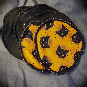 May include: Four black fabric circles with a yellow fabric circle with black cat silhouettes and stars printed on it in the center. The black circles have a frayed edge.