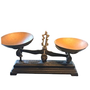 Peut inclure: Une balance à plateaux vintage dotée d'une base lourde en fonte noire et d'une colonne de support centrale verticale. Deux plateaux circulaires et peu profonds en métal cuivré sont suspendus de chaque côté du fléau central pivotant.