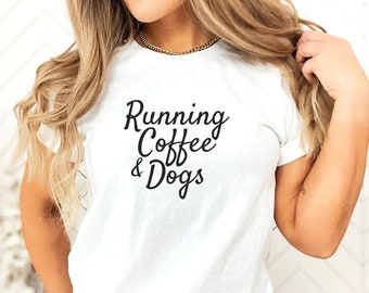 May include: A white short-sleeved t-shirt featuring the black text Running Coffee & Dogs printed in a cursive script font on the chest. The shirt is paired with light blue acid-wash denim jeans that have a visible silver metal button at the waist.
