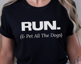 May include: A black short-sleeved t-shirt featuring the white text "RUN." in a bold, sans-serif font, followed by the text "(& Pet All The Dogs)" in a smaller, white serif font centered on the chest area of the garment.