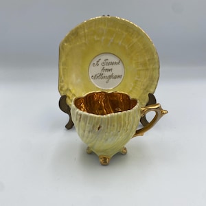 May include: A yellow teacup and saucer set with gold detailing. The teacup has a textured exterior and a gold interior. The saucer has a scalloped edge and the text "A Present from Nottingham".