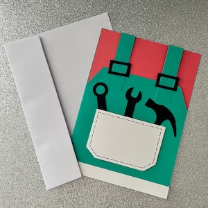 May include: A green and red card with a paper cutout of a tool belt with tools. The tool belt has a white pocket with a dashed line border.