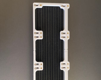 May include: A rectangular computer component with a black, grid-like interior and a white frame. The frame has multiple mounting points with gold-colored accents. The component is designed for cooling and measures approximately 10 inches in length.
