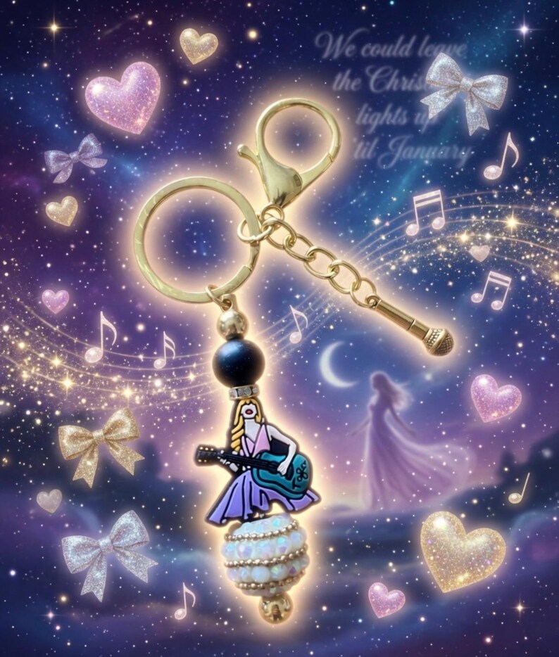 May include: A gold-toned keychain with a charm featuring a woman playing a guitar, a microphone, and a black bead. The charm is adorned with a white and opalescent bead. The background has musical notes, hearts, bows, and text that reads "We could leave the Christmas lights up til January."