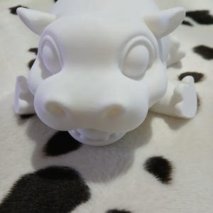 May include: White ceramic figurine of a cartoon hippopotamus with large eyes and a wide open mouth. The hippopotamus is lying on its belly with its legs outstretched.