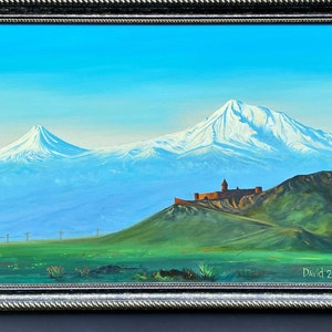 Puede incluir: Una pintura de una cordillera con un pico nevado y una fortaleza en una colina en primer plano. El cielo es azul y las montañas son verdes y marrones. La pintura está enmarcada en un marco negro.