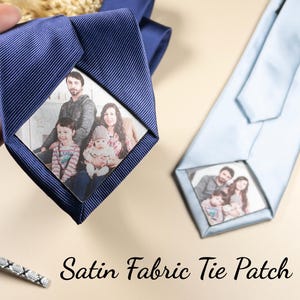May include: Navy blue satin tie with a family photo patch. A light blue tie with a family photo patch is also visible. A silver tie clip is at the bottom left. The text "Satin Fabric Tie Patch" is at the bottom.