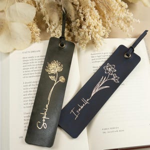 May include: Two leather bookmarks. One is dark green with a gold chrysanthemum and the name "Sophia". The other is navy blue with a white daffodil and the name "Isabella". Both have a leather loop for easy use.