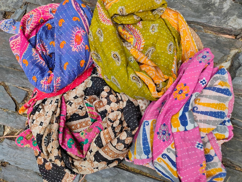 May include: Four colorful kantha quilts with intricate patterns in shades of pink, blue, green, and brown. The quilts are made of recycled saris and are hand-stitched with kantha embroidery.
