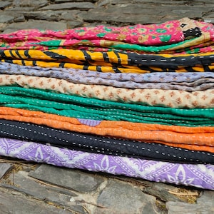 Puede incluir: Una pila de colchas kantha de colores con varios patrones y costuras. Las colchas est&aacute;n hechas de saris reciclados y son una artesan&iacute;a tradicional india.