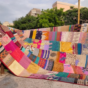 Könnte beinhalten: Ein farbenfroher Patchwork-Quilt mit rotem Rand, im Freien ausgestellt. Der Quilt besteht aus verschiedenen Stoffstücken in Rosa-, Gelb-, Blau- und Lilatönen. Der Text "Missy Classy Studio" ist auf dem Quilt zu sehen.