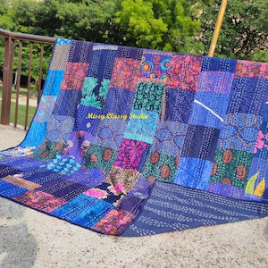 Könnte beinhalten: Eine rechteckige Patchwork-Decke mit verschiedenen blauen, violetten und rosafarbenen Stoffquadraten mit unterschiedlichen Blumen- und Geometriemustern. Die Decke zeigt sichtbare weiße Steppstiche und den Text Missy Classy Studio.