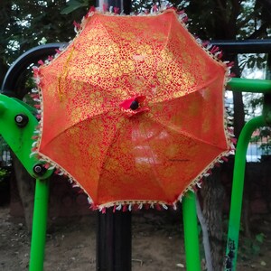 May include: A red and gold patterned umbrella with white fringe hanging from a black pole.