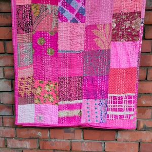 May include: A pink and purple patchwork quilt with a variety of floral and geometric patterns. The quilt is made of recycled saris and is hand-stitched.
