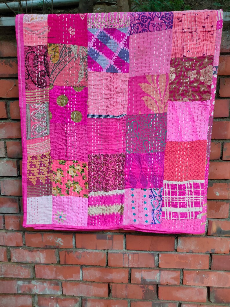 May include: A pink and purple patchwork quilt with a variety of floral and geometric patterns. The quilt is made of recycled saris and is hand-stitched.
